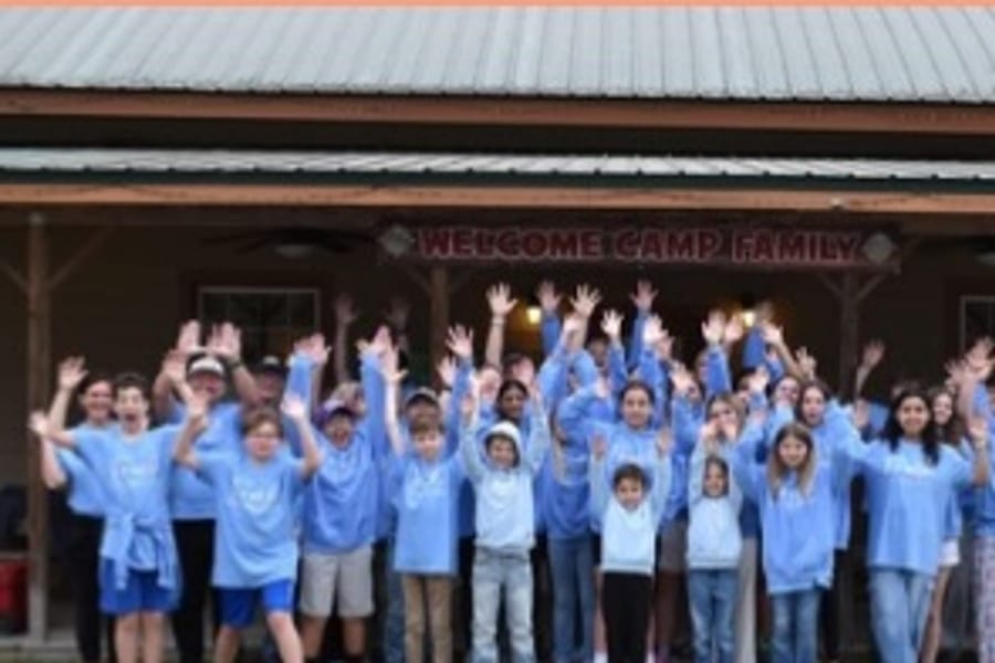 Kids in matching camp shirts with their hands in the air under a Welcome Camp Family banner